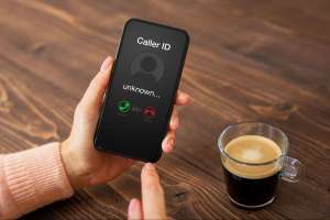 A person holding a smartphone showing an incoming call from an unknown number, representing the can you hear me phone scam. A person holding a smartphone showing an incoming call from an unknown number, representing the can you hear me phone scam.